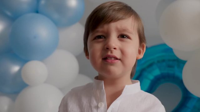 boy of two years in a white shirt sitting at home in blue balloons
