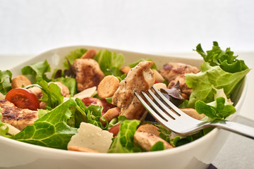 A cesar salad and a chunk of chicken in a fork