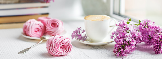 Bouquet of lilacs, cup of coffee, homemade marshmallow and stack of books on window sill Romantic spring morning.