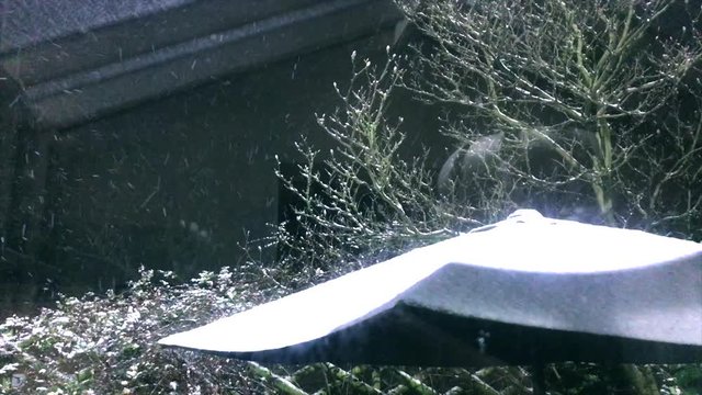 Snow falling on outdoor table umbrella under a layer of snow