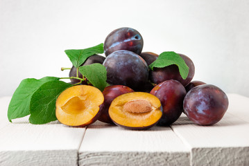 Plums on white wooden background. Half of blue plum fruit. Many beautiful plums with leaves.