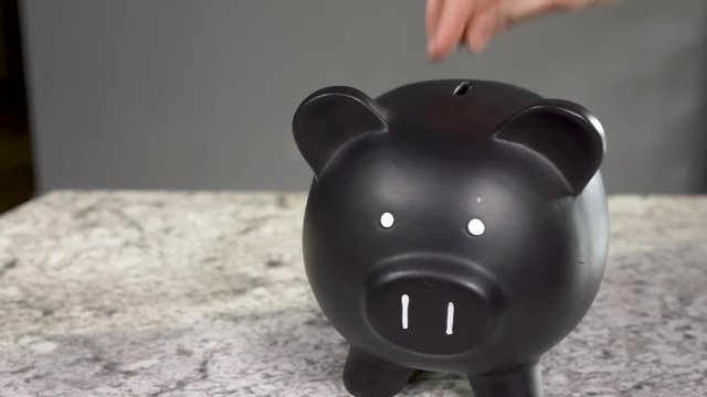 Woman putting coins in black piggy bank