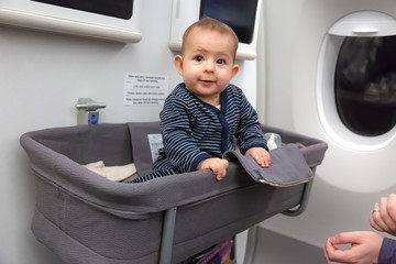 Infant girl sit in special baby bassinet in airplane. She is laugh and amazed, it is her first...
