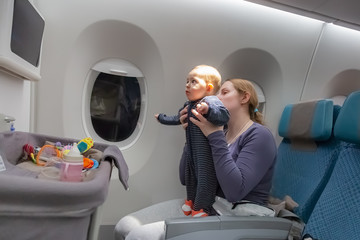 Infant plays on mother hands at the airplane.  Amazed of tablet monitor and flight.  Plane baby bassinet on the foreground