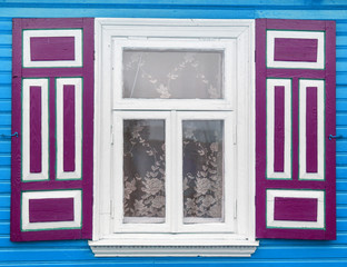 Vintage blue paint wall with transparent glass window and decorative violet purple shutter. Wooden rustic window frame in small cottage house. 