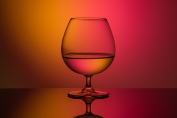 close-up of brandy glass with liquid on orange red background