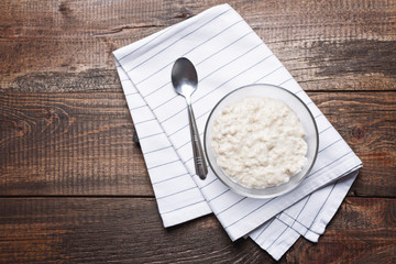 Oatmeal with spoon on cloth napkin on brown wooden background, top view