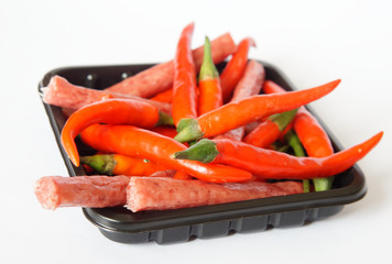 Red chili peppers and thin Bavarian sausages in a black backing on a white background