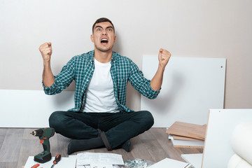 angry man sitting on the floor with instructions for assembling furniture