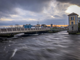 Motion Blur Shot of Rapid Water Flowing Under a Bridge in the City of Galway Ireland - with a Cloudy Sunset in the Background