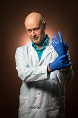 Experienced doctor 50s wearing a white coat, wearing blue rubber gloves and smiling