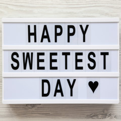 'Happy Sweetest Day' word on modern board over white wooden background, top view. From above, flat lay, overhead.