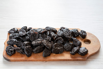 Dry prunes on rustic wooden board on a white wooden table, side view. Copy space.
