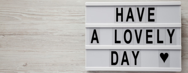Modern board with text 'Have a lovely day' on a white wooden surface, top view. From above, flat lay, top view. Copy space.
