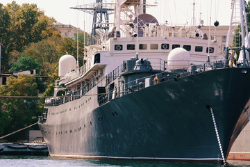 Close-up of the bow of black ship moored in the port at sunset with trees and mountains in the...