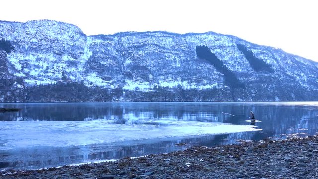 Fly Fishing cast in Norwegian fjord. Fisherman stanging inside water with mountains in the background. Slow motion.