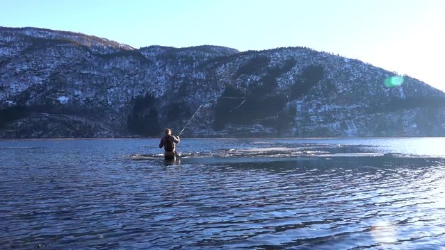 Fly Fishing cast in Norwegian fjord. Man standing in water with ice flakes floating infront of him. Slow motion.