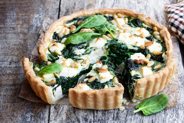 Vegetarian spinach tart with feta and pine nuts on wooden table