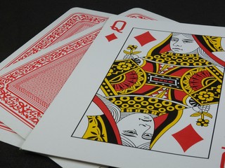 Three playing cards on a black surface. The Queen of Diamonds is facing up. The back of the cards is red.