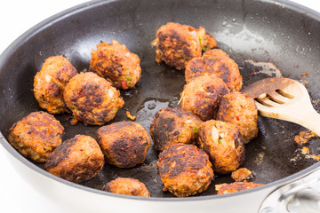 Meatballs Sizzling in Hot Skillet with Slotted Wooden Spatula