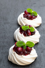 Mini Pavlova meringue nests with cranberry and mint leaves on black stone background