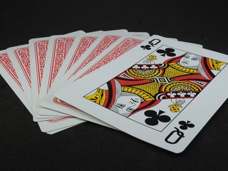A few playing cards on a black surface. The Queen of Clubs is facing up. The back of the cards is red.