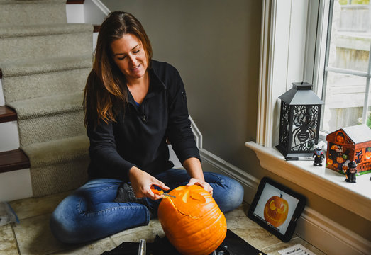 Woman carving pumpkin while making jack o' lantern at home during Halloween
