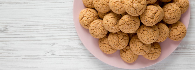 Top view, almond cookies on pink plate over white wooden surface. Flat lay, overhead, from above. Copy space.