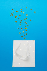 White gift paper bag with stars and confetti from it over blue background