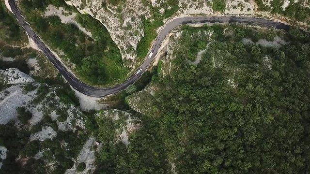 Two Cars driving on a mountain pass. Filmed from top bird's eye view with a drone circling around them smoothly. Like in GTA game. Summer atmosphere in green forrest und grey rocky french alps