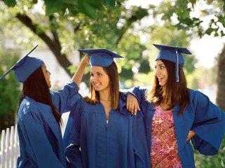 Portrait of three high school girls wearing caps and gowns. 