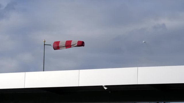 An isolated windsock blowing in strong winds at an airfield and an aircraft taking off in the background.