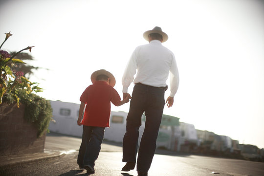Rear view of a father and a son walking on the road.