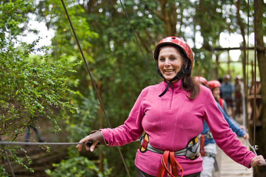 Smiling mid-adult woman walking across a wooden suspension bridge in a forest.