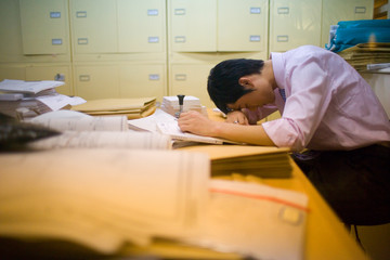Young adult businessman sleeping with his head down on a desk in an office.