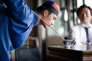 Young adult man dressed in traditional clothing doing a tea ritual in a cafe.