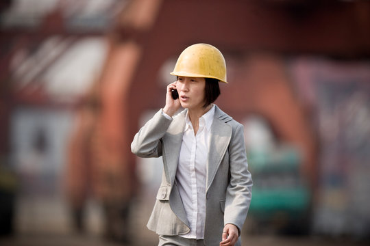 Mid-adult business woman talking on a cellphone while wearing a hard hat in a construction site.