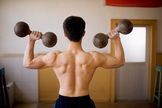 Young adult boy lifting dumbbells in a gym.