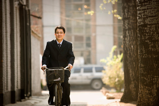 Portrait of a mid-adult businessman riding a bicycle down a street.