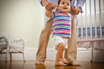 Toddler being helped to walk by his father.
