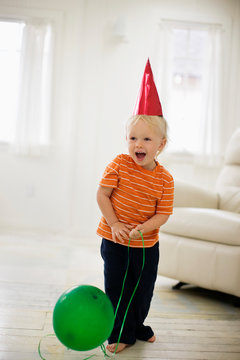 Toddler wearing a party hat with a balloon.