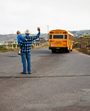 Father and son waving goodbye to school bus