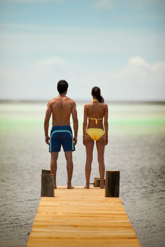 Young couple look out at the ocean while standing on a pier.