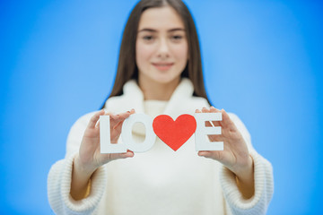 Young pretty girl dressed in white clothes. During this time it stands on a blue background. Holds a word of love in hands.