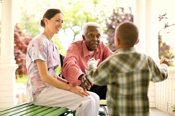Nurse looks on happily as a senior man puts out his arms to hug a boy who is running to him for an embrace.