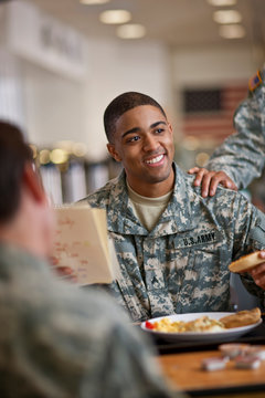 Young soldier smiles happily as he reads a letter over breakfast in the army mess hall.