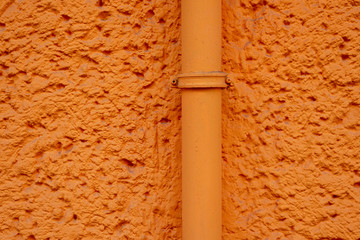 Orange verputzte Hauswand mit Rohrleitung