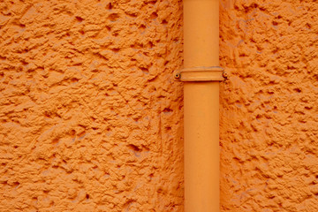 Orange verputzte Hauswand mit Rohrleitung