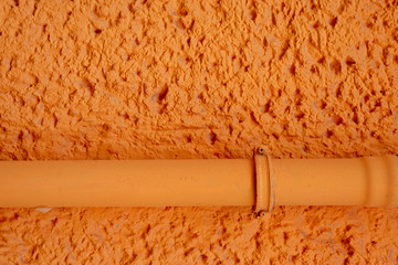 Orange verputzte Hauswand mit Rohrleitung