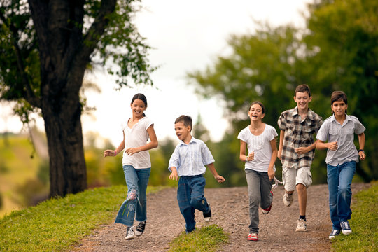 Small group of children running together over gravel road.